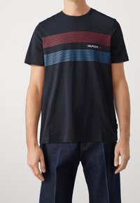 Camiseta de algodón navy de manga corta, con rayas horizontales rojas y azules y el texto "HILFIGER '85". Cuello redondo clásico.