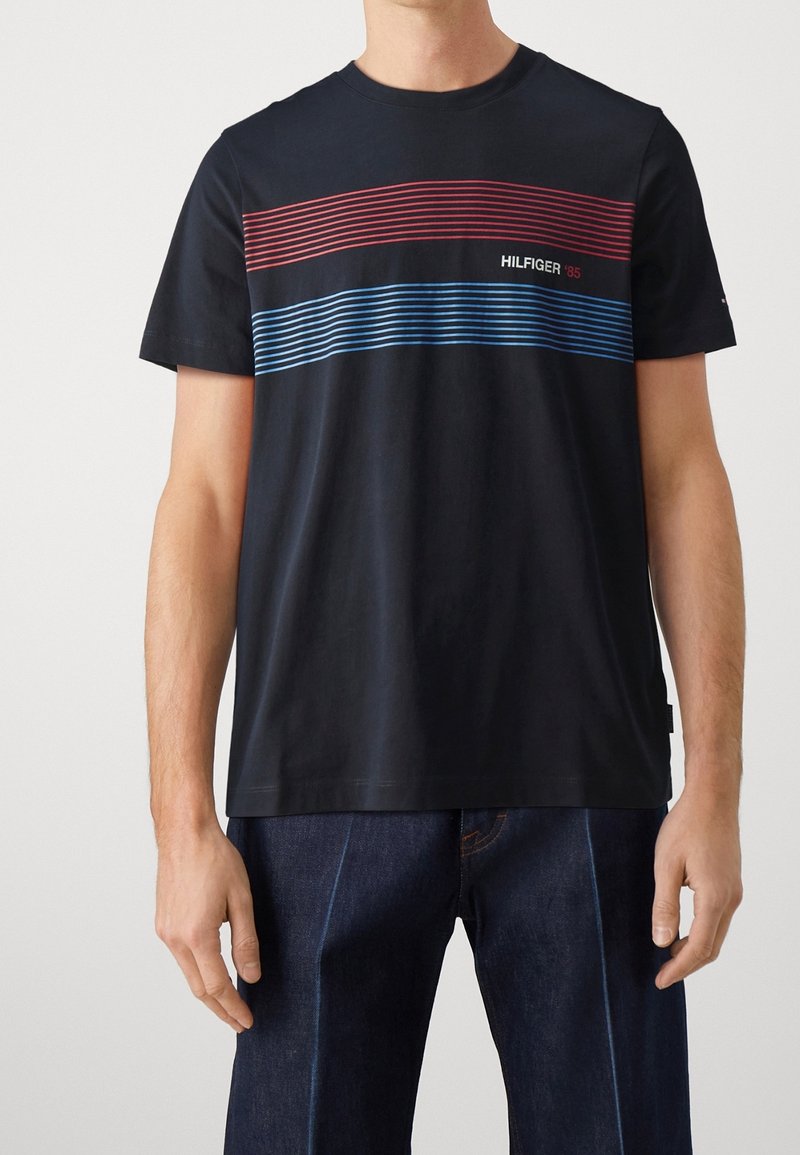 Camiseta de algodón navy de manga corta, con rayas horizontales rojas y azules y el texto "HILFIGER '85". Cuello redondo clásico.