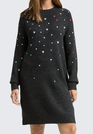 Femme portant une robe en tricot à manches longues gris foncé avec de petits motifs de cœurs et de points blancs, gris et rouges.