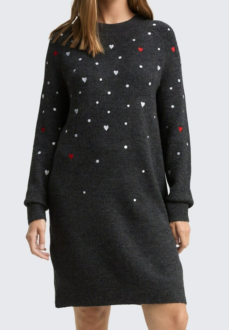 Femme portant une robe en tricot à manches longues gris foncé avec de petits motifs de cœurs et de points blancs, gris et rouges.