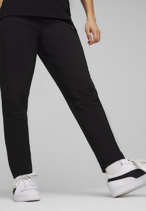Black athletic pants with a tapered fit, made from soft fabric, featuring side seams and a simple design. Worn with white sneakers.