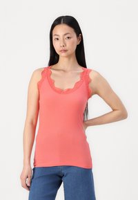 Top de tirantes de coral con ribete de encaje en la parte del cuello y los brazos, diseño ajustado, combinado con unos vaqueros de mezclilla azul. Sin patrones visibles ni elementos metálicos.