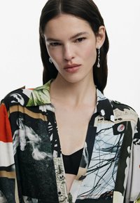 Chemise à manches courtes en impressions mixtes, présentant des couleurs vives comme le rouge, le noir et le vert. Fabriquée en tissu lisse avec un col et des détails de boutons.