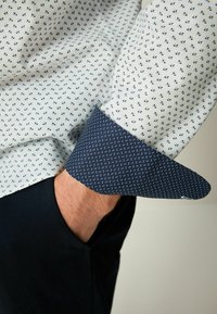 Camisa de vestir de algodón con base blanca y pequeños patrones de hojas azules, puños en azul oscuro con diseño de puntos y corte entallado.