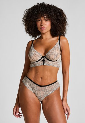 Lace lingerie set in nude met zwarte afwerking. De beha heeft een beugel en een strik aan de voorkant; de bijpassende slip heeft een golvend ontwerp en een bloemenpatroon.