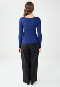 Długi rękaw, niebieska ribbed bluzka połączona z szerokimi czarnymi spodniami, charakteryzującymi się gładką teksturą i dopasowanym krojem.