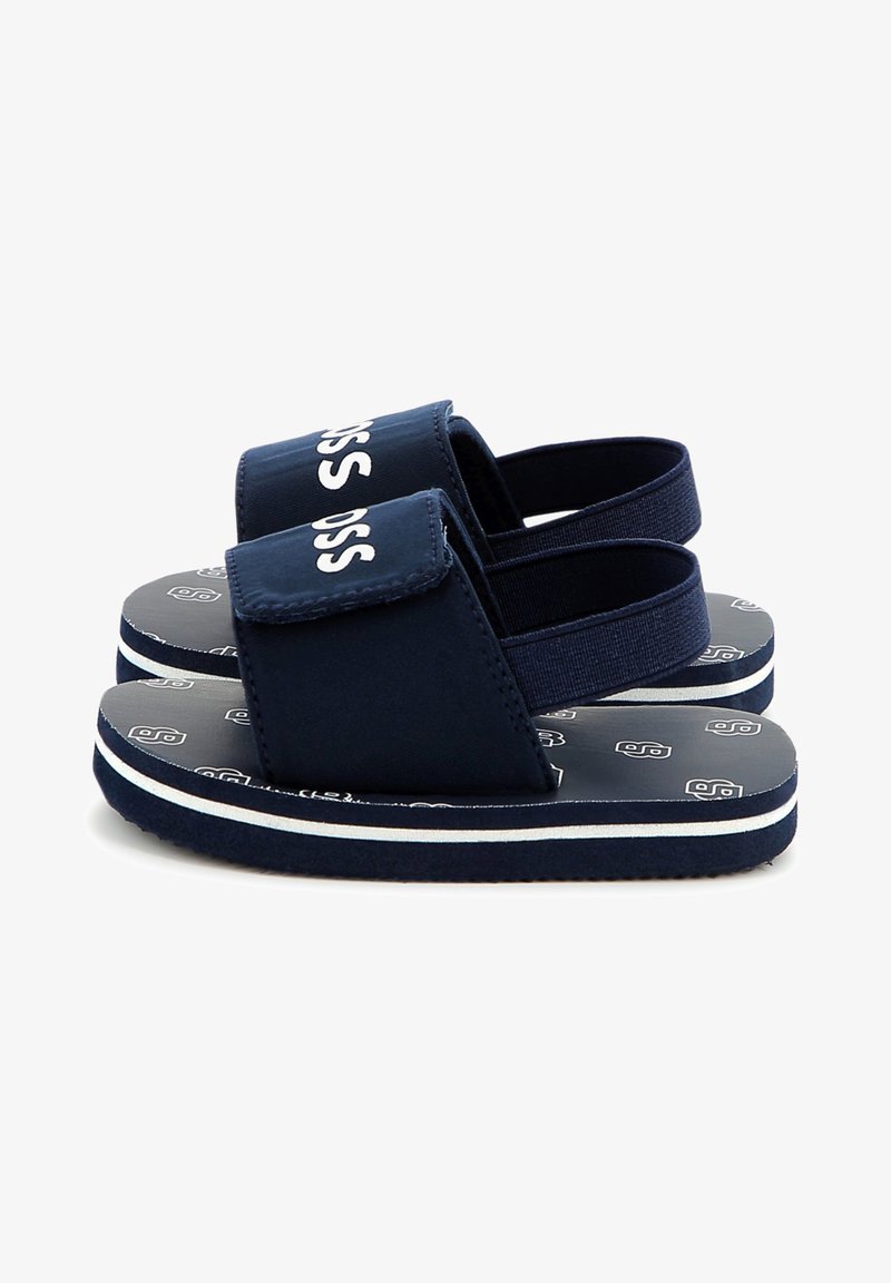 Sandali blu navy con una fascia spessa e chiusura in velcro. La suola in gomma testurizzata presenta una striscia bianca. Il design include un motivo del logo sulla soletta.