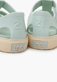 Light blue rubber sandals with open design, textured strap, and a cream-colored sole. Features embossed number "21" and logo patch.