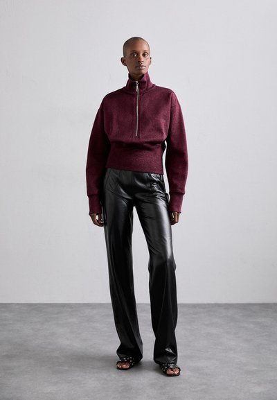 Bordo zip-up megztinis su aukštu apykakle ir raukšlėmis, derinamas su blizgiais juodais odiniais plačiais kelnėmis ir atvirais juodais sandaliukais.