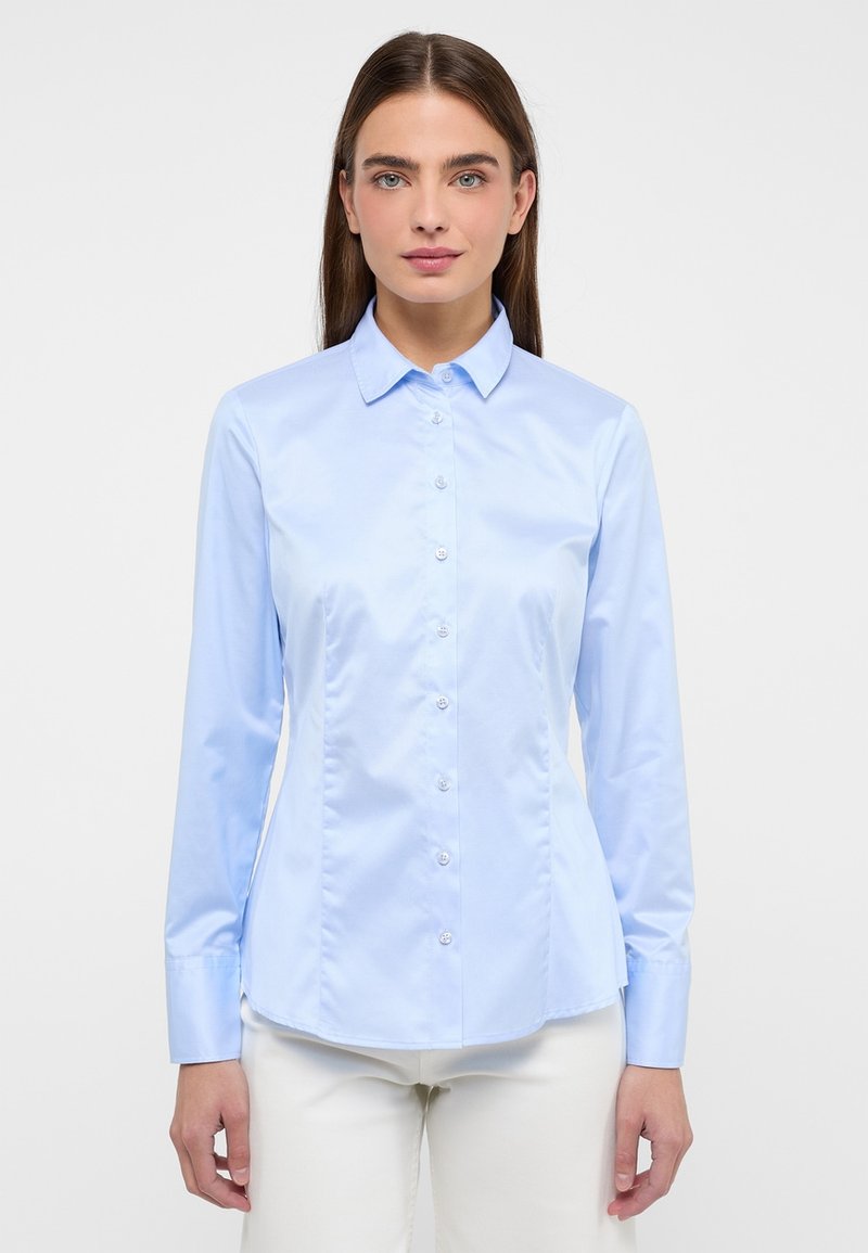 Camicia azzurra chiara con colletto a punta, maniche lunghe e forma aderente. Realizzata in tessuto liscio e lucido con una leggera lucentezza.