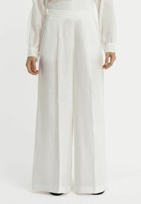 Pantalons larges blancs en tissu léger, dotés d'une taille haute, de plis sur le devant et de poches latérales. Texture lisse avec un design épuré.