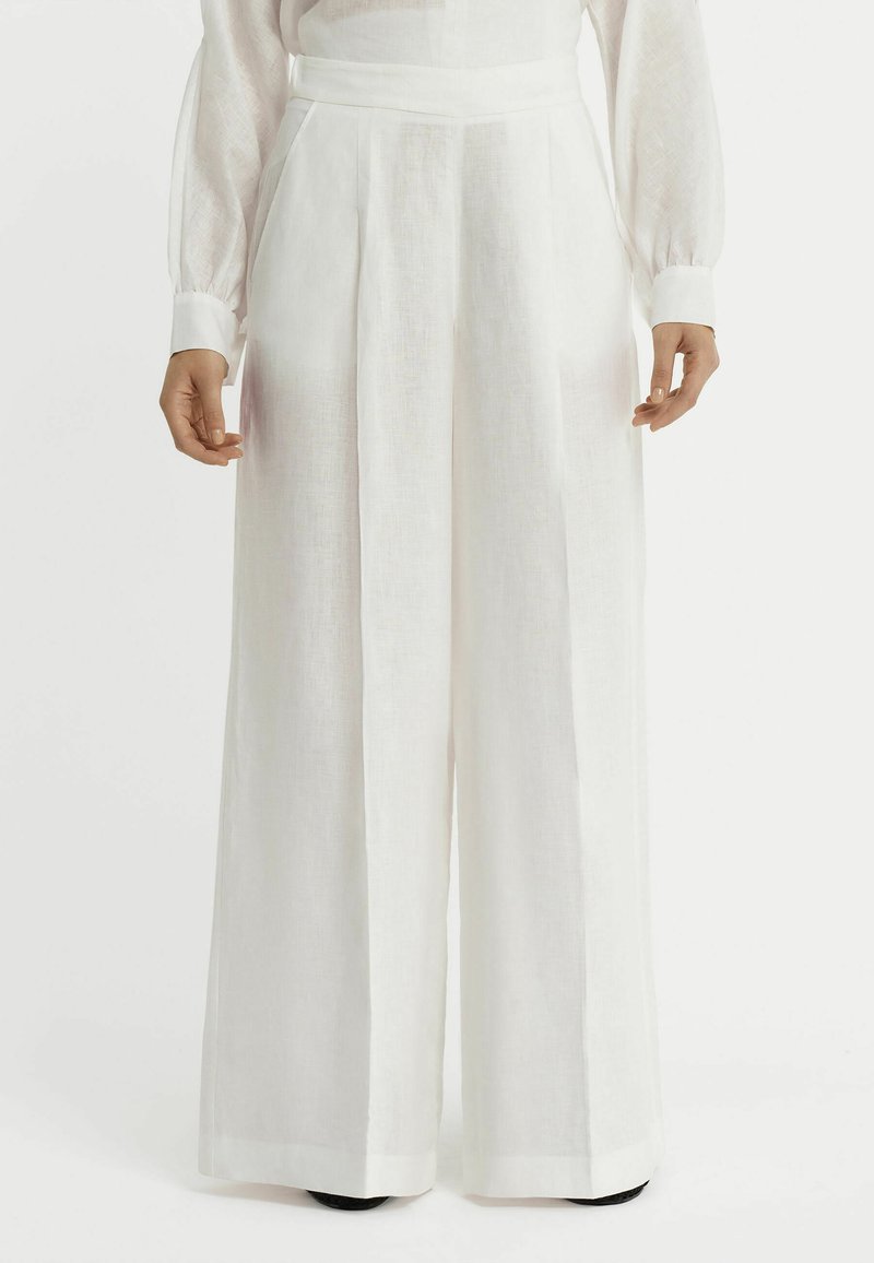 Pantalons larges blancs en tissu léger, dotés d'une taille haute, de plis sur le devant et de poches latérales. Texture lisse avec un design épuré.
