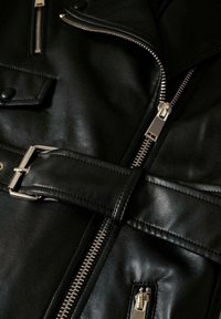 Veste en cuir noire avec fermeture éclair argentée, ceinture avec boucle, poche à rabat boutonnée et petite poche zippée.