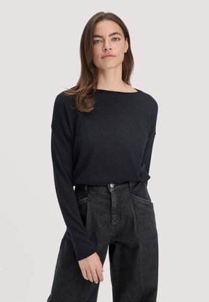 Langärmliges schwarzes Oberteil aus weichem Stoff mit weitem Ausschnitt, kombiniert mit hochgeschnittenen, dunkelblauen Jeans mit Fronttaschen.