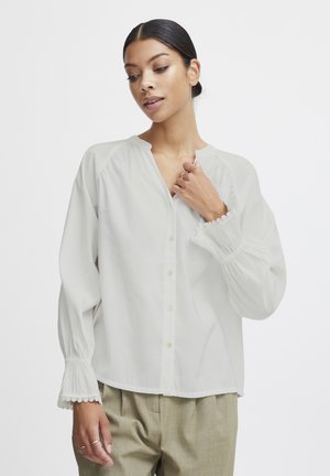 Witte blouse met een iets openstaande kraag en knopen aan de voorkant. Heeft lange mouwen met elastische manchetten en kantafwerking, gemaakt van lichte stof.