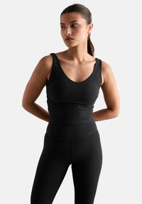 Czarny dopasowany crop top z szerokimi ramiączkami i głębokim dekoltem, zestawiony z czarnymi legginsami z wysokim stanem; gładki, elastyczny materiał na całej powierzchni.