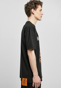 Camiseta negra de gran tamaño con un estampado gráfico en el frente, mangas cortas y una etiqueta naranja en el dobladillo con detalles de la marca.