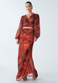 Abito a due pezzi rosso e nero a fantasia con maniche lunghe, top avvolgente e gonna con spacco alto. Realizzato in materiale leggero e fluido.
