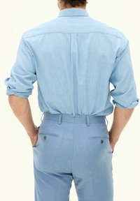 Camicia in misto lino di colore azzurro chiaro con maniche arrotolate. Pantaloni azzurro chiaro con due tasche posteriori dotate di chiusura a bottone e una texture liscia.