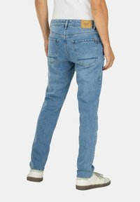 Jeans de mezclilla azul claro con corte recto, que cuentan con dos bolsillos traseros, una etiqueta de cuero marrón en la cintura y un cierre de cremallera.