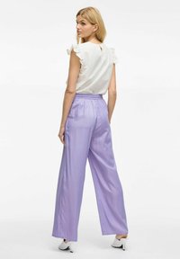 Witte gerimpelde top met een open rugdetail, gecombineerd met lavendel satijnen wijde broek. De broek heeft een elastische tailleband en een gladde structuur.