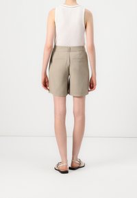 Khaki šortky s bočními kapsami, upravený střih a hladká textura. V kombinaci s bílým bezrukávovým topem a plochými sandály.
