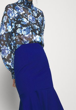 Blumenbluse mit blauen und weißen Rosen auf schwarzem Hintergrund, kombiniert mit einem blauen knielangen Rock. Durchscheinender Stoff und Detail mit hochgeschlossenem Ausschnitt.