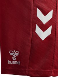 Rote Shorts aus strukturiertem Stoff mit weißen Chevron-Streifen an der Seite und einem kleinen eingestickten "hummel"-Logo unten.