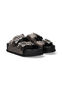 Sandalias metálicas plateadas trenzadas con dos correas anchas, adornadas con hebillas de strass, apoyadas en una suela gruesa negra.