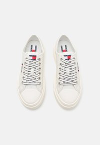 Baskets en toile blanches avec bout rond, lacets gris et accents cousus. Présente des détails de logo sur la languette et sur le côté. Texture lisse.