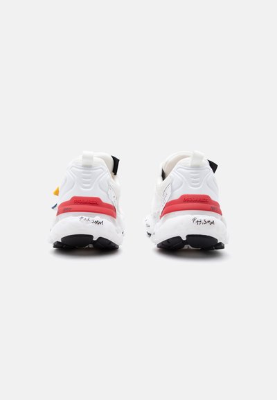 Λευκά αθλητικά παπούτσια με κόκκινες λωρίδες και μαύρες σόλες, ορατά από πίσω, με το όνομα της μάρκας και κείμενο σε χειρόγραφο στυλ στις μεσαίες σόλες.