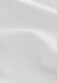 Tissu blanc lisse avec des plis subtils et une texture fine visible sous un éclairage doux.