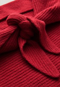 Maglione rosso lavorato a maglia con trama a coste e dettaglio a fiocco sul colletto, che presenta un aspetto soffice e accogliente.