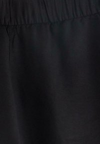 Tessuto nero con una texture liscia e una vita elastica arricciata. La superficie appare opaca con sottili variazioni alla luce.