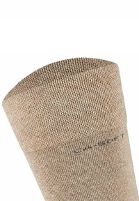 Calcetín beige con una textura acanalada y un borde superior liso. Presenta costuras a lo largo de la banda y un pequeño texto impreso cerca del puño.