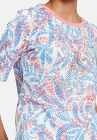 Vit kortärmad skjorta med blommönster i blått och rosa, med en kontrasterande rosa halsringning och dekorativa rhinestones på framsidan.