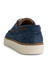 Zapato de ante azul marino con un acento de cuero color cuero alrededor del cuello, superficie texturizada y suela de goma blanca con un sutil patrón de agarre.