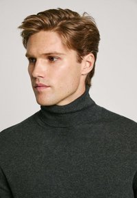 Maglione a collo alto grigio scuro realizzato in un tessuto a maglia morbido e strutturato, con un design aderente e sottili dettagli a coste al collo.