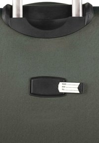 Maleta rígida con exterior texturizado en verde oscuro, con asa de transporte negra y soporte para etiqueta con etiqueta blanca.