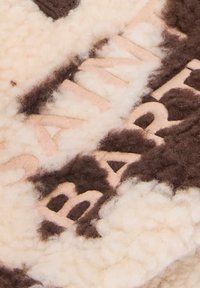 Il tessuto in misto lana presenta uno sfondo crema con accenti e testo marrone, incorporando una superficie morbida e testurizzata con dettagli ricamati.