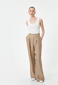 Pantalones de lino ligeros de color beige, con corte amplio y pliegues. Combinados con una camiseta ajustada blanca, creando un look simple y monocromático.