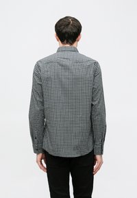 Fekete-fehér kockás hosszú ujjú ing, hegyes gallérral és begombolt mandzsettákkal. A hátulnézet testhezálló szabást és finom textúrát mutat.