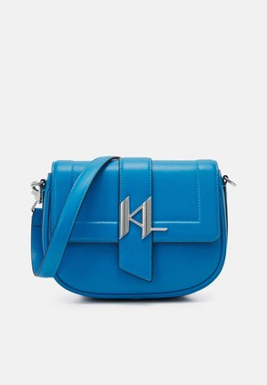 Blauwe leren crossbodytas met zilveren geometrische gesp en verstelbare band op een effen lichte achtergrond.