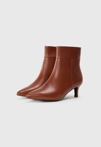 Bottes de cheville en cuir marron avec un bout pointu et un petit talon. Texture lisse, coutures minimales et design contemporain épuré.