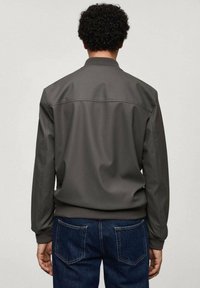 Chaqueta bomber gris hecha de material liso, con cuello acanalado, mangas largas y puños elásticos, combinada con vaqueros azules.