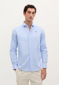 Camicia button-up blu chiaro con un sottile motivo a quadri, maniche lunghe, colletto a punta e un piccolo logo blu navy sul petto. Tessuto liscio.