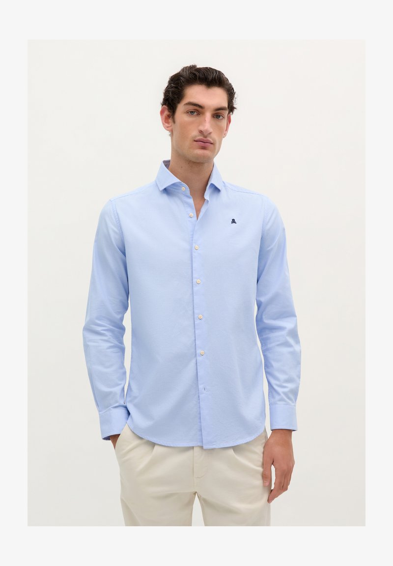 Cămașă albastră deschisă, cu un model discret în carouri, mâneci lungi, guler ascuțit și un mic logo bleumarin pe piept. Textură netedă.