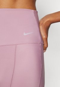 Heledat roosad kõrge vöökohaga retuusid, mis on valmistatud siledast, elastset materjalist. Omavad väikest halli Nike logo ja nähtavaid õmbluse detaile.