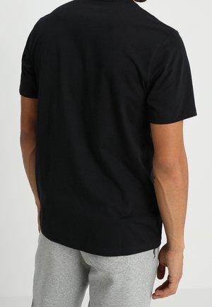 Camiseta de algodón negra con mangas cortas, escote redondo y un corte relajado, mostrada por la parte de atrás sobre un fondo neutro.