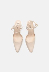 Escarpins à bout pointu beige avec une finition lisse et brillante, brides de cheville fines et un design minimaliste. Comprend une semelle intérieure rembourrée.